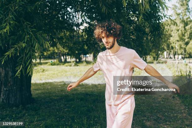 portrait of a young man 20 years old with curly hair in a pink t-shirt on a tree background - 20 24 years 個照片及圖片檔