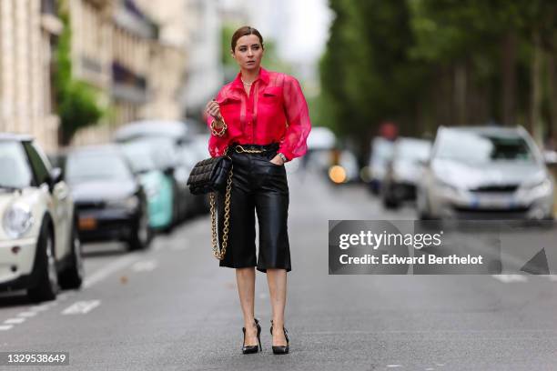 Julia Comil wears a raspberry pink sheer blouse / shirt in organza and raw silk, black faux leather high waisted long Bermuda shorts by Nanushka,...