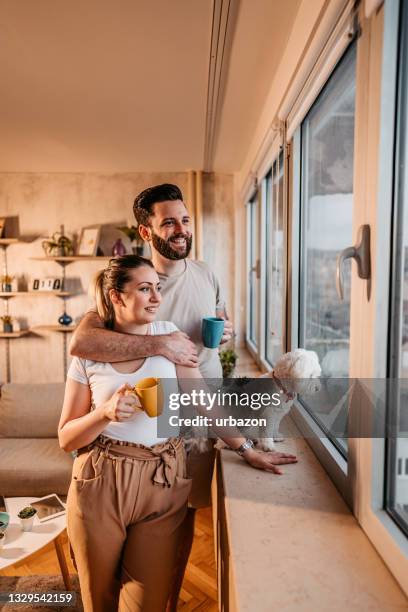 young couple and dog looking through the window in their home - 年輕情侶 個照片及圖片檔