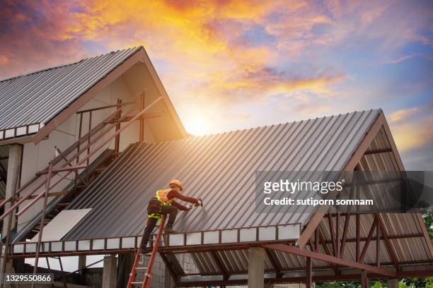 roofer working installing metal sheet roofing with sunset background - roofing stock-fotos und bilder