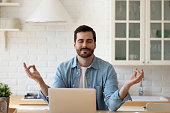 Calm man meditating with eyes closed in kitchen near laptop
