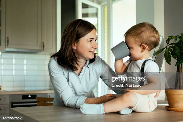 mujer joven con su lindo bebé divirtiéndose en la cocina - baby cup fotografías e imágenes de stock