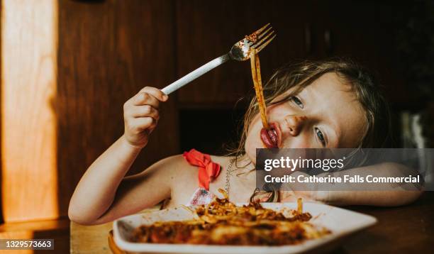 tired little girl messes around while eating spaghetti bolognese - kauwen stockfoto's en -beelden