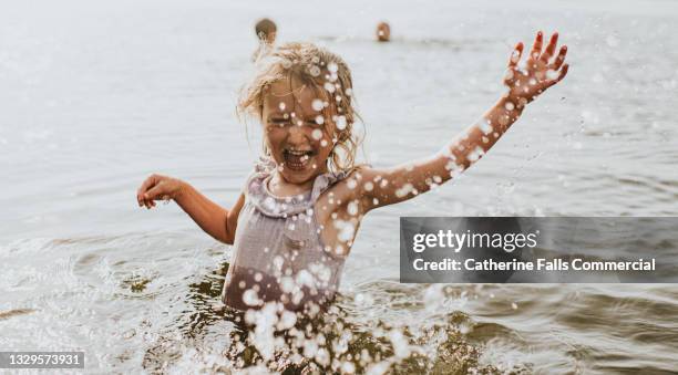 mischevious little girl in a lake intentionally splashes the photographer - droplet sea summer stockfoto's en -beelden