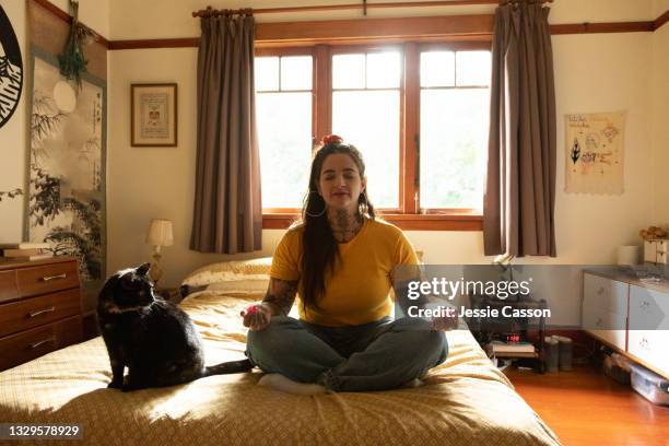 tattooed woman sitting on bed meditating with cat - black hair dresser stock pictures, royalty-free photos & images