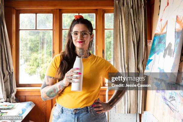 woman standing in home art studio and drinking from a reusable drink bottle - bottle illustration vintage stock-fotos und bilder