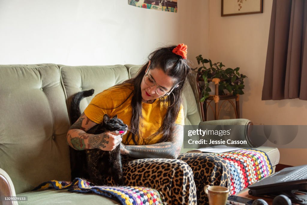 Tattooed woman sitting on a sofa holding a cat
