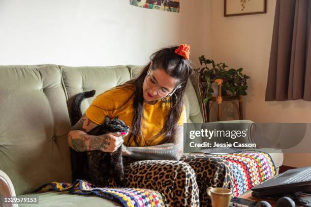 tattooed woman sitting on a sofa holding a cat - cat attitude stock pictures, royalty-free photos & images