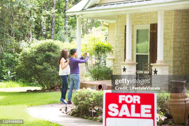 mid adult couple are considering purchasing a new home.  for sale sign in foreground. - real estate sign 個照片及圖片檔