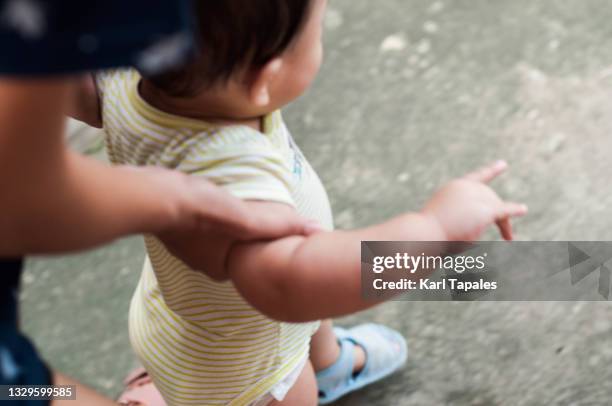 a southeast asian baby boy is learning to walk with the assistance of his mother in the backyard - life events ストックフォトと画像