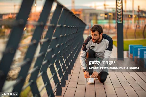 lacing up before hitting the road. man is preparing for running over the bridge. - tiersport stock pictures, royalty-free photos & images