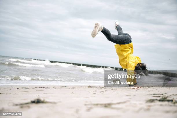 little girl in yellow raincoat doing cartwheel at beach - mecklenburg vorpommern 個照片及圖片檔