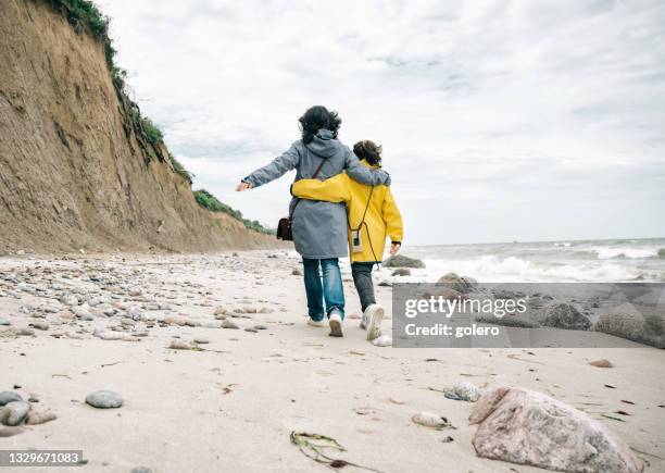 kleines mädchen in gelbem regenmantel, das mit mutter am steinstrand umarmt geht - mecklenburg vorpommern stock-fotos und bilder