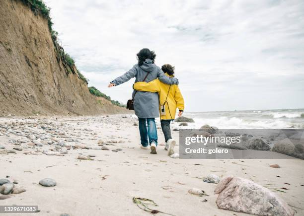 little girl in yellow raincoat walking embraced with mother on stone beach - mecklenburg vorpommern 個照片及圖片檔