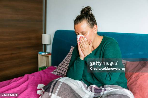 unwell woman sneezing into tissue in home environment - caucasian woman sick in bed coughing stock pictures, royalty-free photos & images