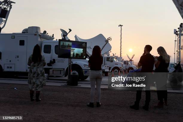 People watch on a television screen as the New Shepard Blue Origin rocket sits on the launch pad before Jeff Bezos along with his brother Mark Bezos,...