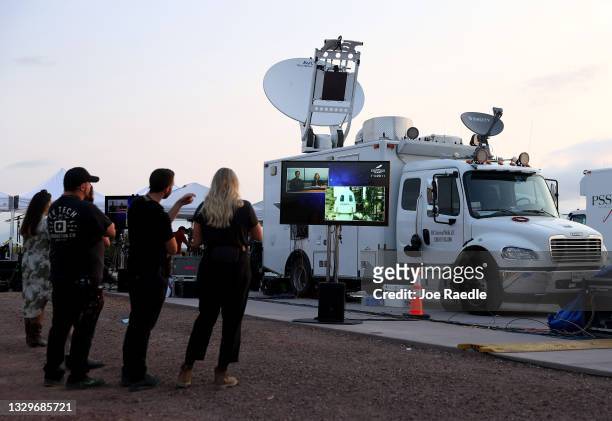 People watch on a television screen as the New Shepard Blue Origin rocket sits on the launch pad before Jeff Bezos along with his brother Mark Bezos,...