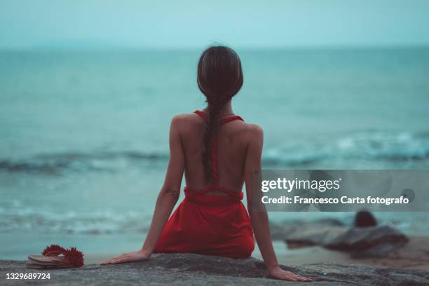 woman with red dress and a braid sits on the seafront. - cinematic stock pictures, royalty-free photos & images