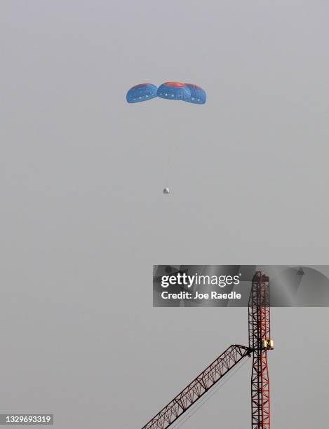 Blue Origin’s New Shepard crew capsule descends on the end of its parachute system carrying Jeff Bezos along with his brother Mark Bezos, 18-year-old...