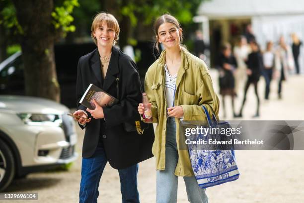 Model wears a beige wool turtleneck pullover, a black oversized blazer jacket, a black shiny leather shoulder bag, gold rings, blue denim jeans...