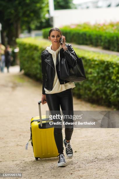 Model wears a yellow pale hoodie sweater, a black shiny leather biker jacket, a black shiny leather large shoulder bag, black leather legging pants,...