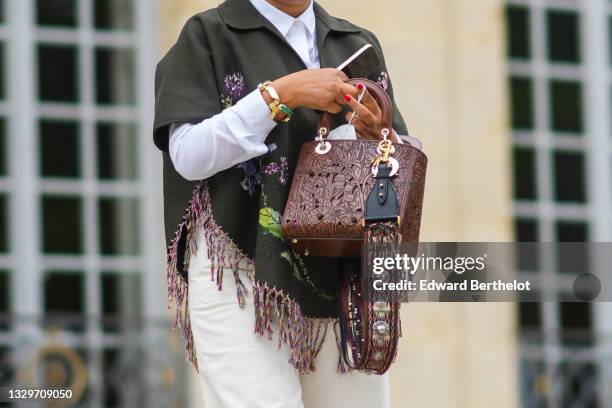 Guest wears a white shirt, a dark green with green and purple embroidered flower pattern and fringed short sleeves coat, white pants, a brown shiny...