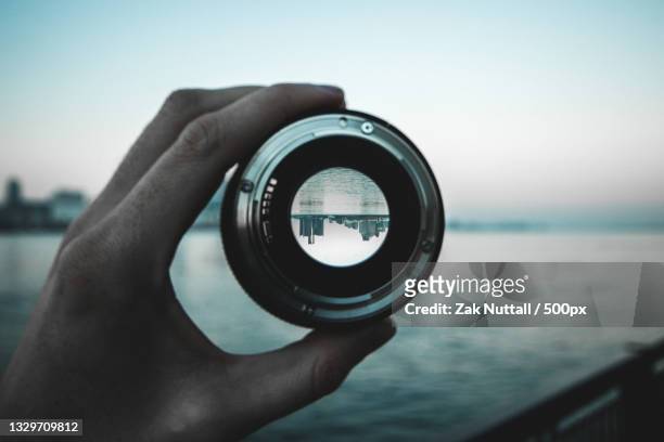 cropped hand holding lens against sea reflecting a cityscape,detroit,michigan,united states,usa - linse stock-fotos und bilder