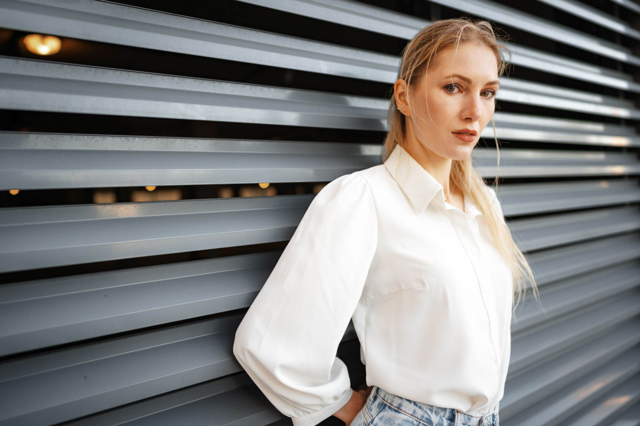 Stylish girl in jeans and white cotton blouse posing near gray wall Stylish girl in jeans and white cotton blouse posing near gray wall