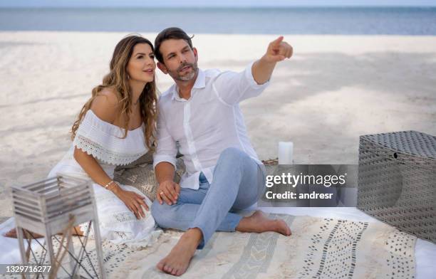 couple having a romantic picnic at the beach and pointing away - romantic picnic stockfoto's en -beelden