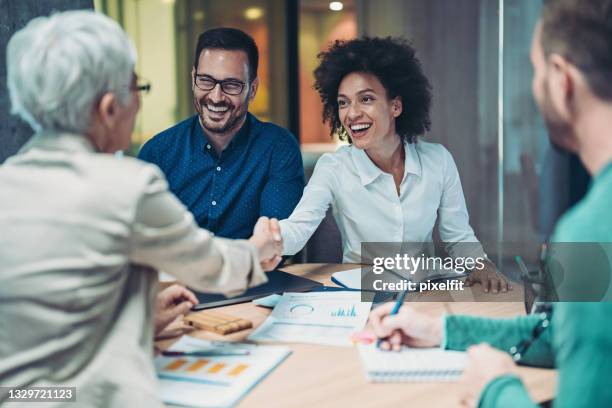 mujeres empresarias sonrientes apretón de manos sobre la mesa - acquisition fotografías e imágenes de stock