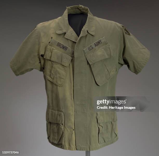 An olive green short sleeve military shirt worn by an African-American soldier during the Vietnam War. This button down style shirt is missing two...