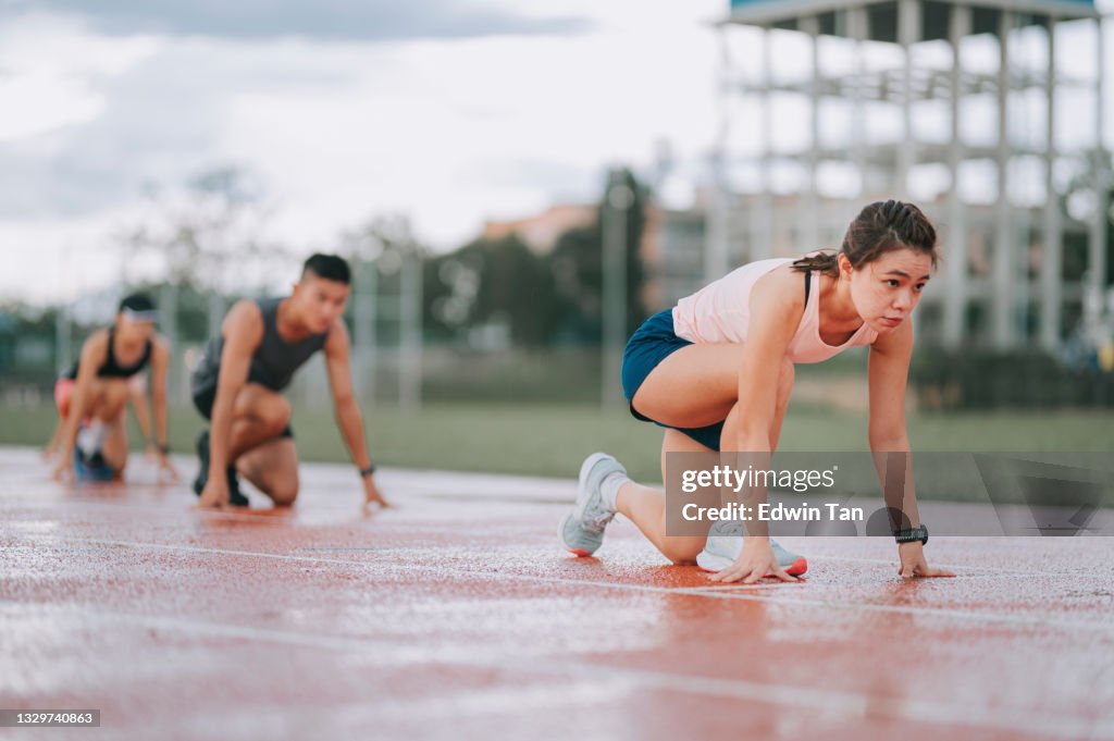 Asian chinese athletes lining up starting line aerodynamic shape getting ready to run at track rainy late evening in stadium