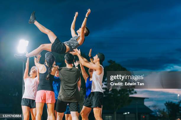 asian chinese athletes cheering throwing lift up their captain winner mid air late evening in stadium - sportteam stockfoto's en -beelden