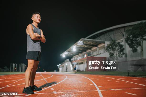 confianza y brazos de atleta masculino satisfechos cruzados mirando hacia otro lado de pie en el estadio de atletismo para todo tipo de clima por la noche - all weather running track fotografías e imágenes de stock