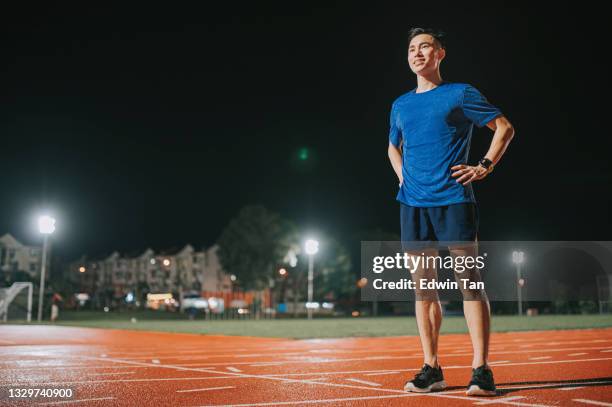 selbstvertrauen und zufriedene männliche athletenhände an den taillenarmen akimbo schaut weg und steht nachts im allwetter-leichtathletikstadion - hand in die hüfte gestemmt stock-fotos und bilder