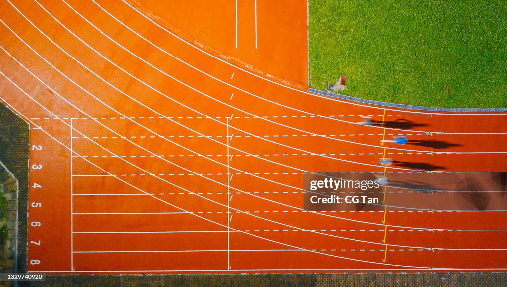 Directly above drone point of view asian chinese male athlete running at men's track rainy late evening in stadium
