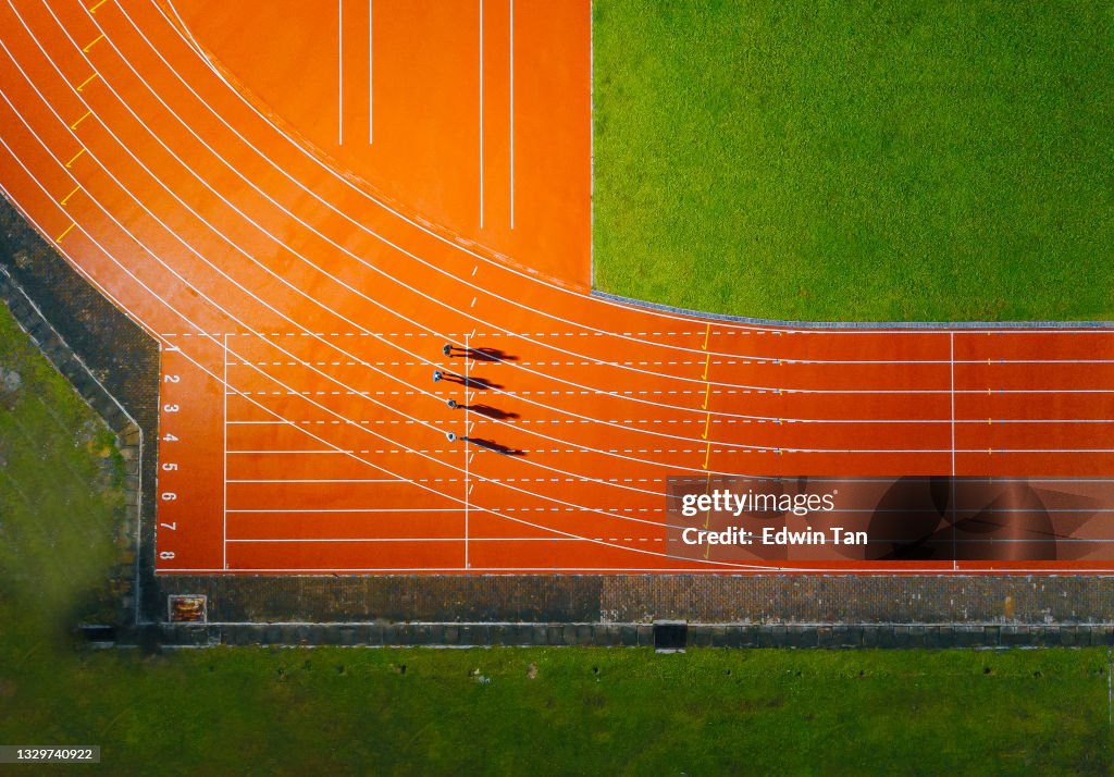 Directement au-dessus du point de vue du drone athlète masculin chinois asiatique courant sur la piste masculine pluvieuse tard dans la soirée dans le stade