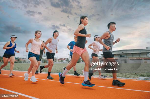 vue latérale l’équipe d’athlètes asiatiques chinois qui court sur le stade d’athlétisme pendant la soirée nuageuse - stade dathlétisme photos et images de collection