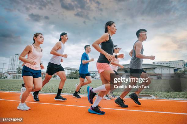 seitenansicht asiatisches chinesisches athletenteam läuft am bewölkten abend im leichtathletikstadion - mixed race stock-fotos und bilder