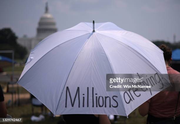 Attendees seek shelter from the sun beneath an umbrella during a COVID-19 prayer vigil on the National Mall honoring and mourning those who have died...