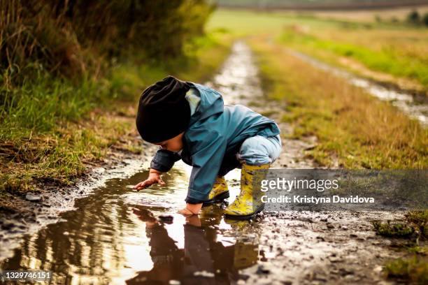 little boy jumping in the water - puddle stock-fotos und bilder