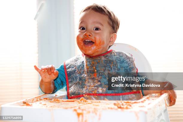 happy baby is eating spaghetti with tomato sauce - happy dirty child stockfoto's en -beelden