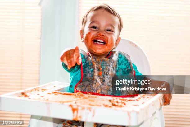 happy baby is eating spaghetti with tomato sauce - scruffy stock-fotos und bilder