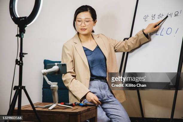 asian woman teaching korean language while live streaming through phone on a tripod - koreaans schrift stockfoto's en -beelden