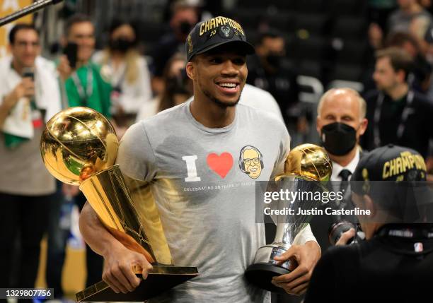 Giannis Antetokounmpo of the Milwaukee Bucks holds the Bill Russell NBA Finals MVP Award and the Larry O'Brien Championship Trophy after defeating...