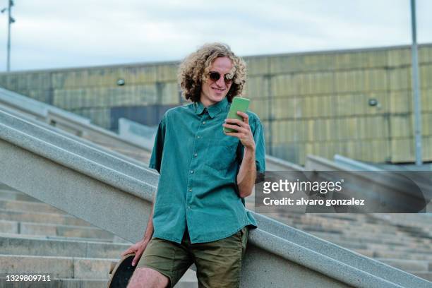young man using smartphone with skate in urban environment - surfar com prancha longa imagens e fotografias de stock