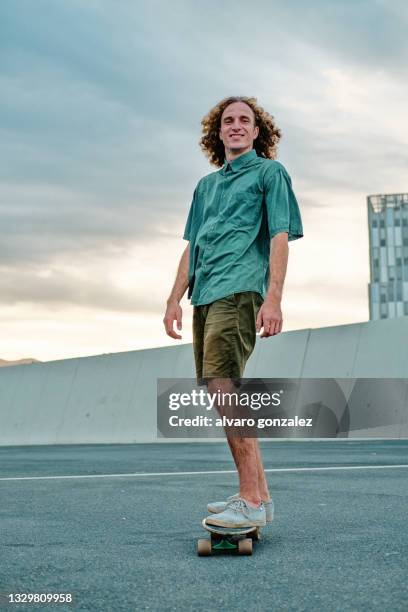 young man smiling and looking at camera using a skateboard - street fashion - fotografias e filmes do acervo