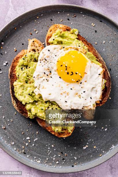 avocado toast with a fried egg and toasted sesame seeds. - avocado stockfoto's en -beelden