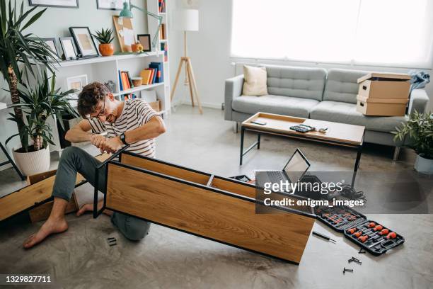 mann in einem neuen zuhause, der möbel für die selbstmontage zusammenbaut - einrichtung stock-fotos und bilder
