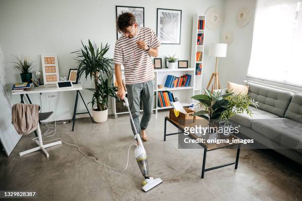 hombre limpiando la casa con aspiradora inalámbrica - vacuum cleaner fotografías e imágenes de stock